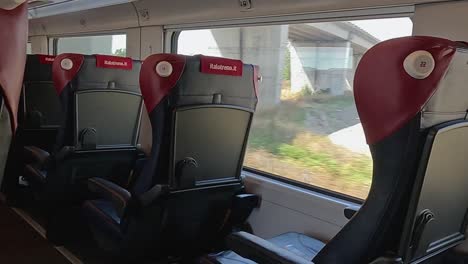 view of sleek train seats with glimpses of rural landscapes through large windows.