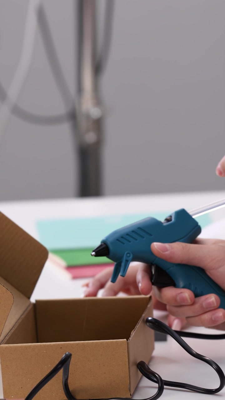Primer plano de manos de estudiante usando una pistola de pegamento caliente en una caja de cartón en la escuela
