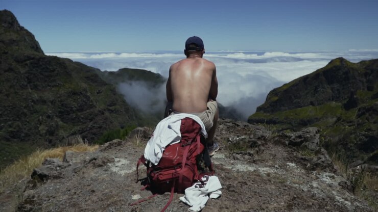 Giovane uomo si riposa su un belvedere panoramico sopra una valle piena di nuvole, al rallentatore.