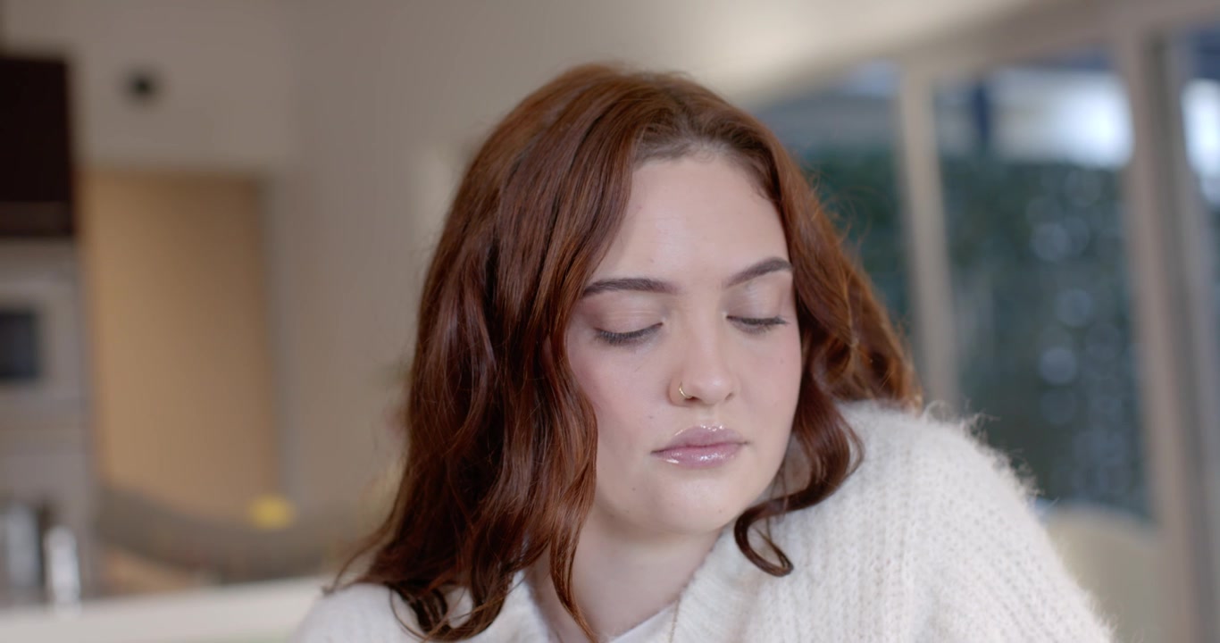 Woman in chunky sweater, nose ring, looking down at table in kitchen, blinking, triggered by object