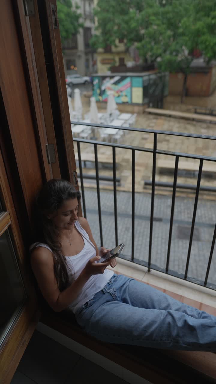 mujer sentada en el balcón, usando el teléfono en un día de lluvia