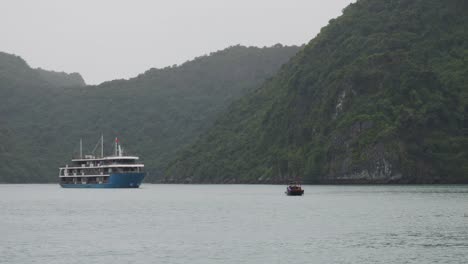 blue cruise ship and small boat on green island background in ha long bay, northeast vietnam