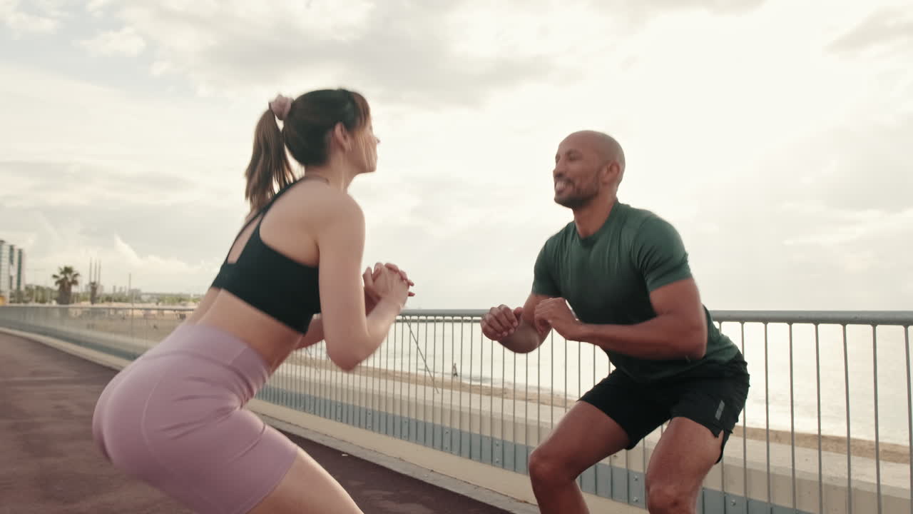 Happy Couple Doing Squats Together on a Coastal Promenade