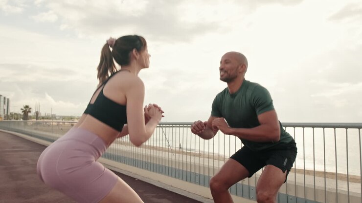 Happy Couple Doing Squats Together on a Coastal Promenade