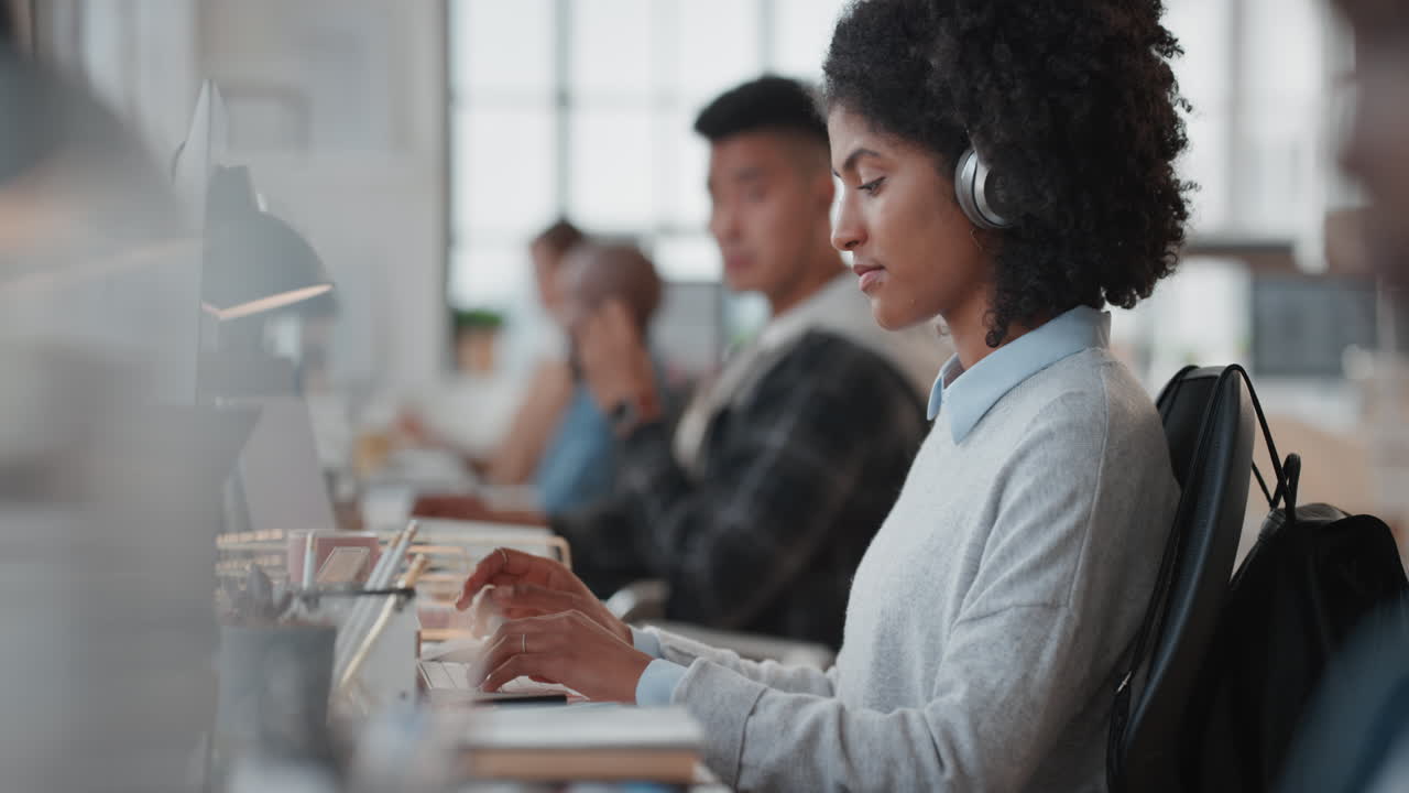 young business woman using computer typing on keyboard sending emails networking online in busy office wearing headphones