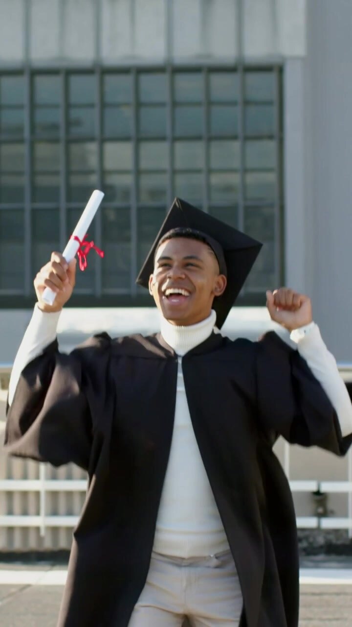 Vertical video: Kissing diploma, grad in gown gold-tassel cap lifting it on roof celebrating degree
