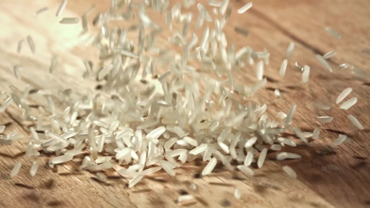 Hvide risgryn falder ned på en træoverflade i slowmotion