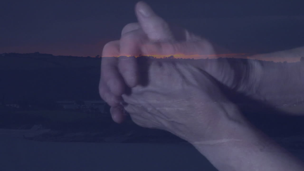 Clasping hands over serene landscape, animation of sunset in background