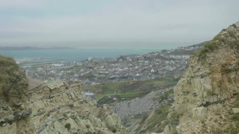 4k cinematic landscape shot of an island town on portland, dorset on a cloudy day, in between two cliffs