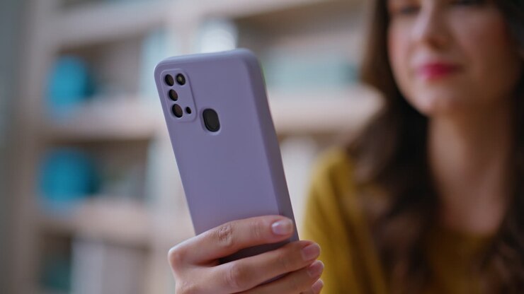 Primo piano di una freelance concentrata sul cellulare, seduta alla postazione di lavoro. Mano di una donna d'affari