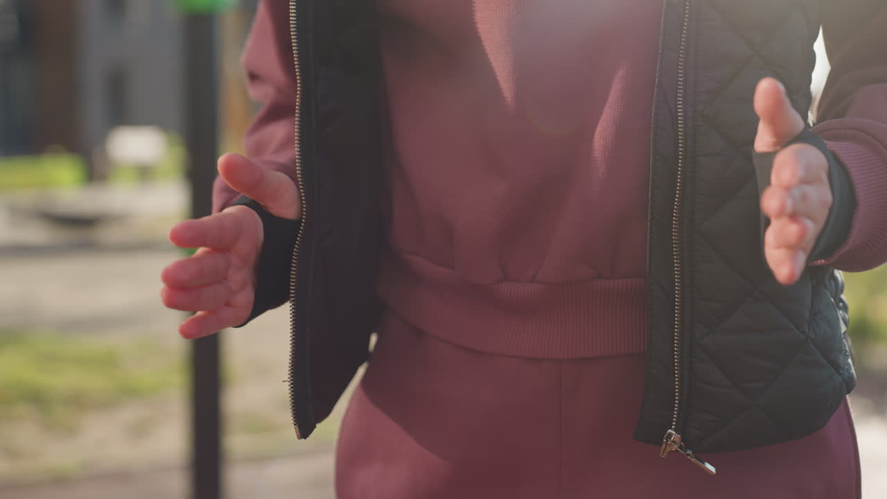 Lower view of jogger in hoodie and vest jogging energetically on urban park pavement surface under morning sunlight, legs and arms moving in rhythmic step for fitness training and warm up session