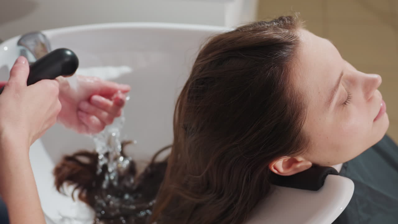Risciacquo professionale con spray lenitivo, una donna si gode un rilassante servizio di shampoo da parte di un tecnico specializzato in capelli, detersione calma e professionale dei capelli con risciacquo delicato e applicazione di spray lenitivo