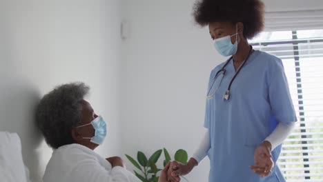 Happy-african-american-female-physiotherapist-helping-senior-female-patient-exercise-at-home