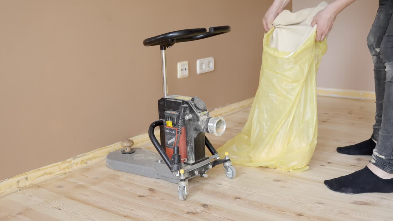 Person emptying dust bag from floor sanding machine into plastic bag