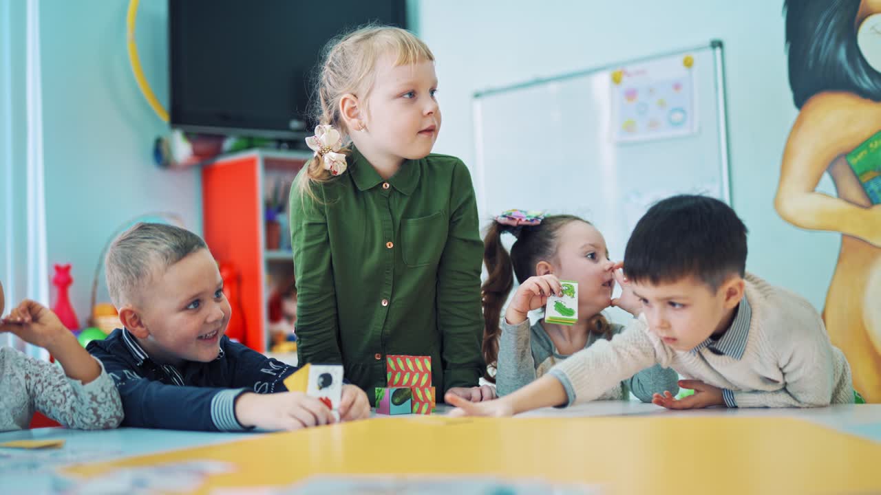 Little boys and girls study in the classroom. Group of small children at the lesson at school. Little kids are studying while playing games at the table with colorful pictures indoors.
