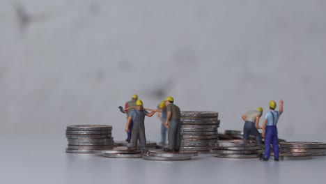 miniature workers working with piles of coins.