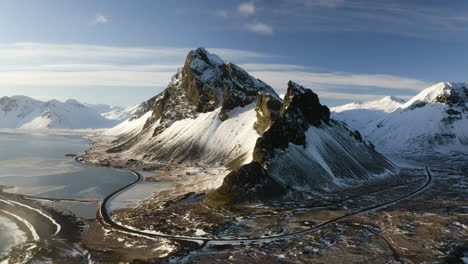 Aerial-view-overlooking-a-snowy-road-and-rocky-peaks,-winter-evening-in-Iceland