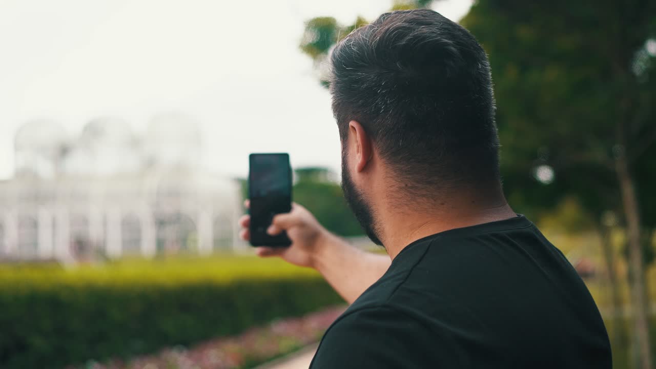 joven tomando una foto del invernadero y el jardín con un celular del jardín botánico, ubicado en curitiba, brasil