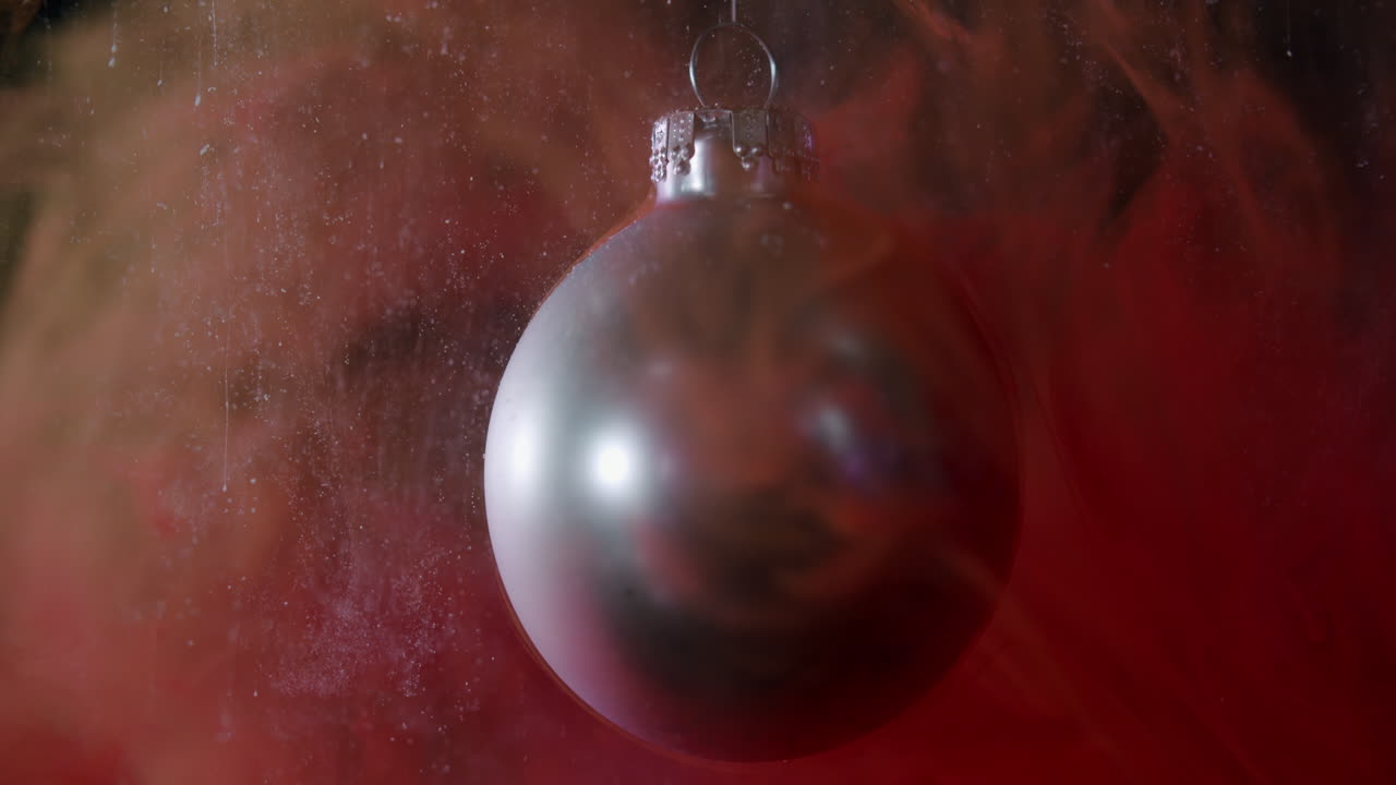 makroaufnahme einer weihnachtskugel mit kleinen rauchpartikeln, die wie schnee aussehen und in zeitlupe darauf fallen