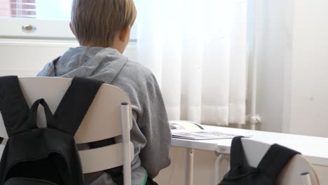 young caucasian school boy sits at a desk and turns to read a book