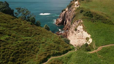 Cinematic-aerial-shot-of-hiker-climbing-path-along-cliff-top-mountain-edge