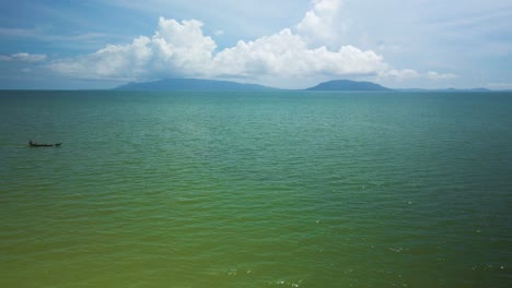 emerald green blue ocean view, island on horizon, small boat travels in sea horizontal enter and exit scene, fluffy clouds in distance