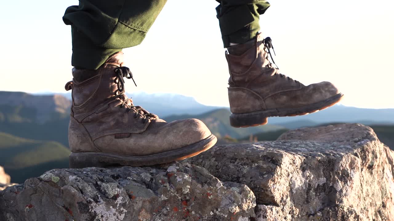 Close-up shot of brown hiker boots stepping on a rock with a mountain blurred background, isolated shot, slow-motion, travel concept