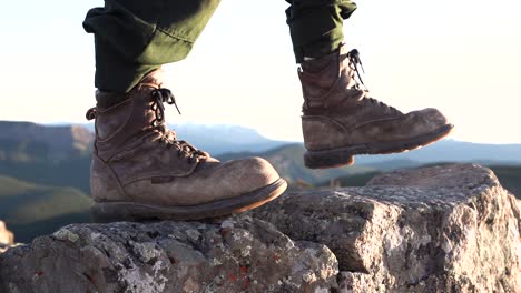 Toma-De-Primer-Plano-De-Botas-De-Excursionista-Marrones-Pisando-Una-Roca-Con-Un-Fondo-Borroso-De-Montaña,-Toma-Aislada,-Cámara-Lenta,-Concepto-De-Viaje