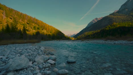 Clear-blue-water-rushing-by-scenic-colorful-autumn-trees-in-the-evening-sun,-Austrian-alps