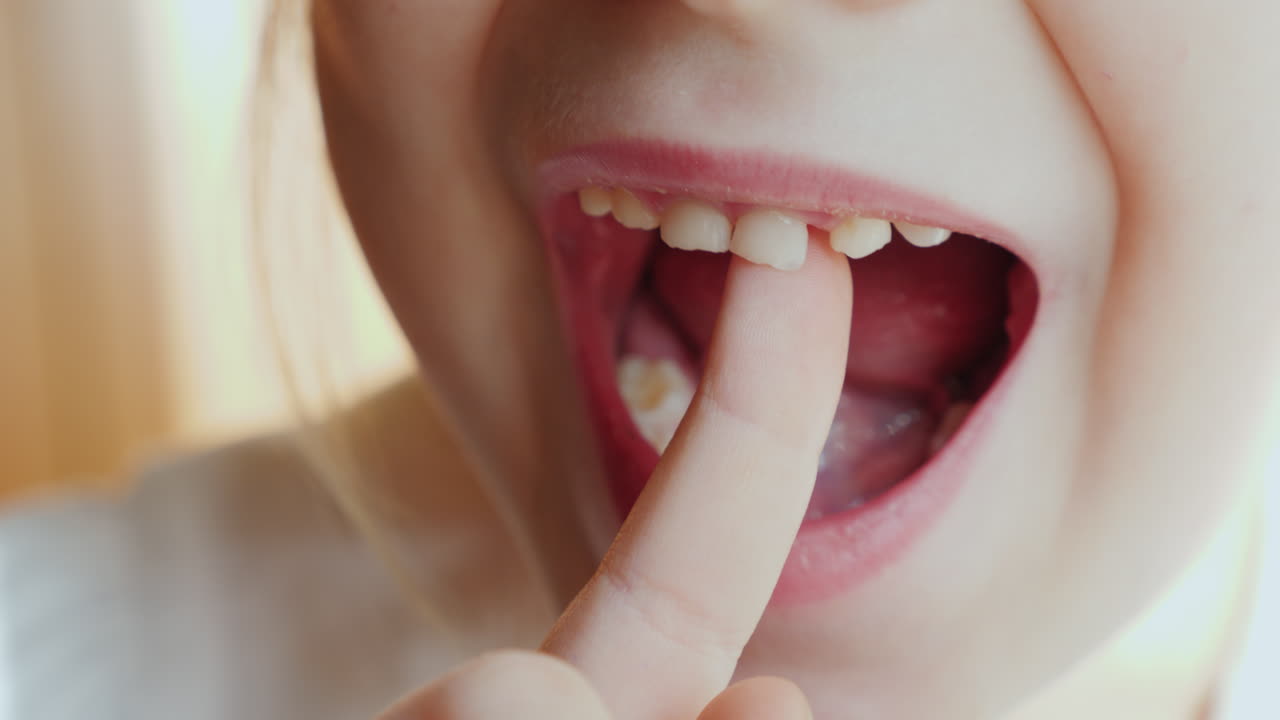 소녀는 곧 빠질 젖니로 손가락을 흔들고 있다