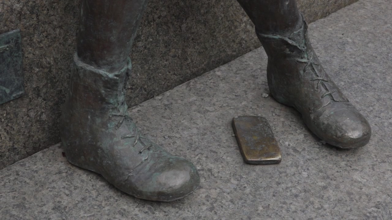 Extreme close up showing a metal mobile phone on a granite pedestal beside boots