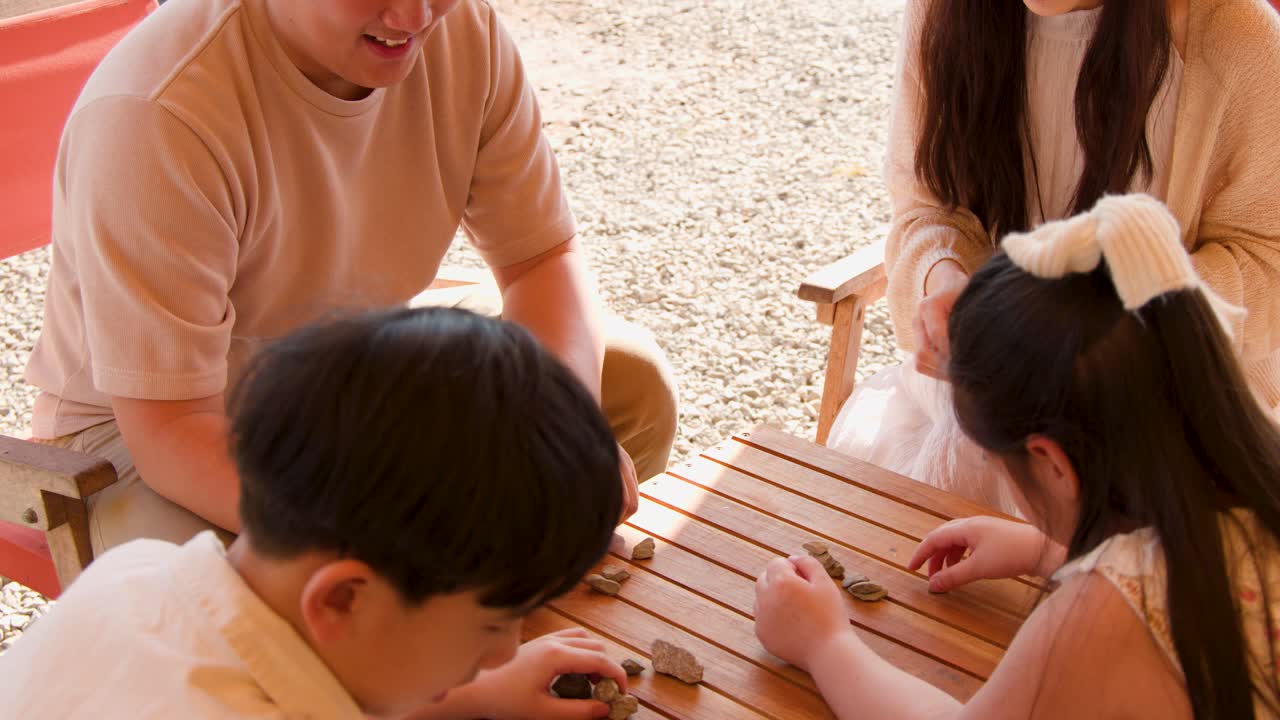 明るい日差しの下、屋外の木製テーブルで親子が石遊びをしている。