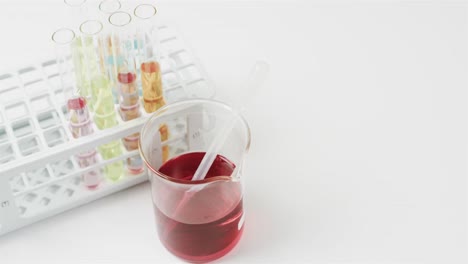 Coloured-liquid-in-flask-with-test-tubes-in-stand-on-white-background-with-copy-space,-slow-motion