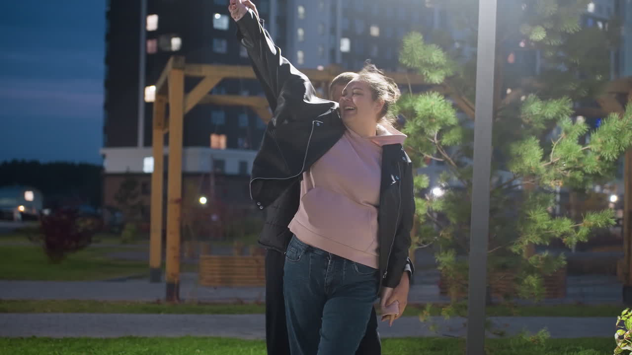 Siblings enjoying happy moment dancing under streetlight with wind blowing trees, capturing joy and carefree dance, illuminated by evening light, playful and fun interaction in urban park
