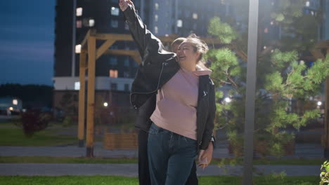 siblings enjoying happy moment dancing under streetlight with wind blowing trees, capturing joy and carefree dance, illuminated by evening light, playful and fun interaction in urban park