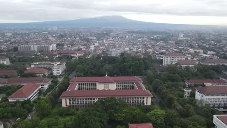 Vista-Aérea-De-La-Ciudad-Y-Grandes-Edificios-De-La-Sala-De-La-Universidad-Gadjah-Mada-Con-El-Monte-Merapi-Al-Fondo