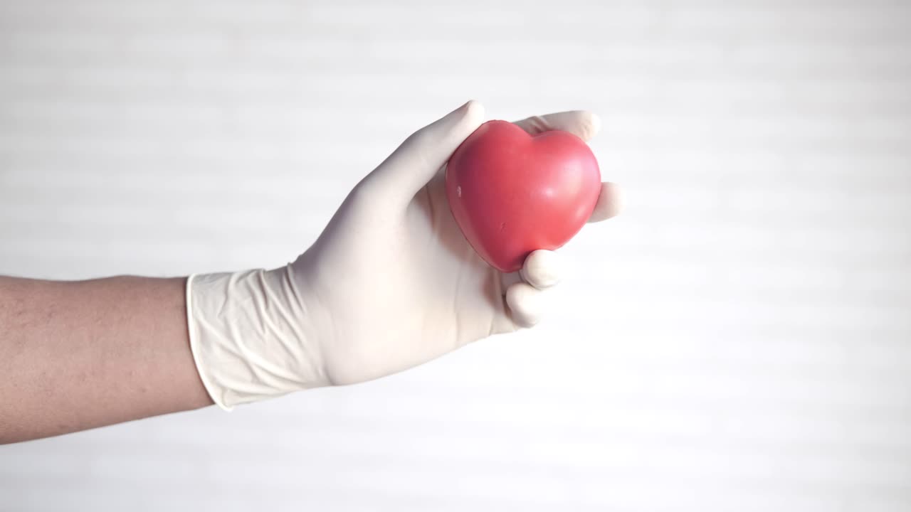 mano con guantes sosteniendo un corazón rojo
