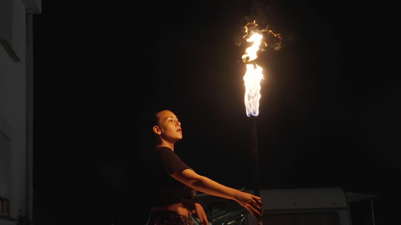 hermosa mujer comedora de fuego mira a la cámara y luego escupe alcohol, queroseno contra la antorcha de fuego y provoca una gran llama