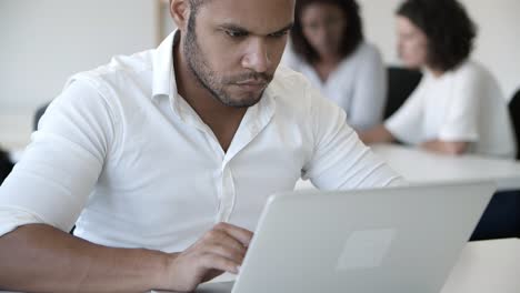 hombre guapo pensativo usando una computadora portátil en una oficina moderna