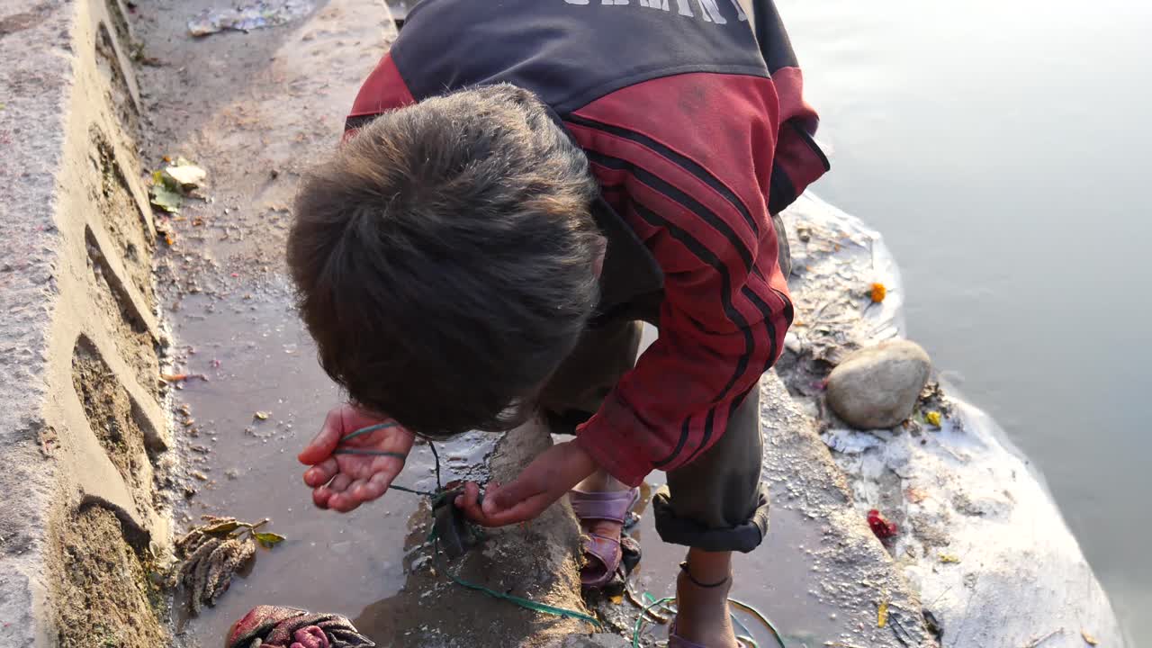 Bambino nepalese che raccoglie denaro usando una calamita durante un festival di digiuno a Sankhu, Nepal