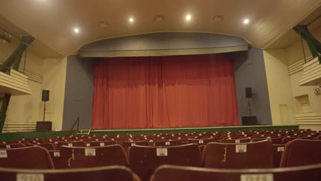 empty red seats in thalia theatre with yellow lights and big red curtain, pov