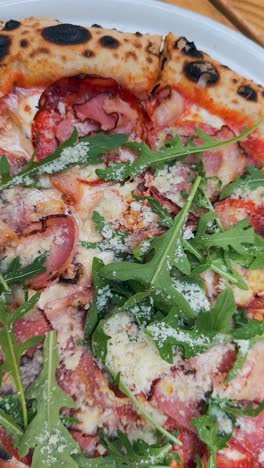 close-up of a delicious pizza with ham, arugula, and cheese