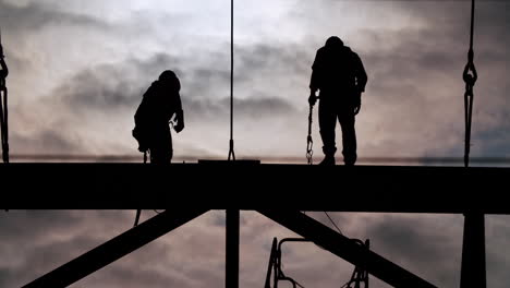 silhouettes of construction workers on a steel beam