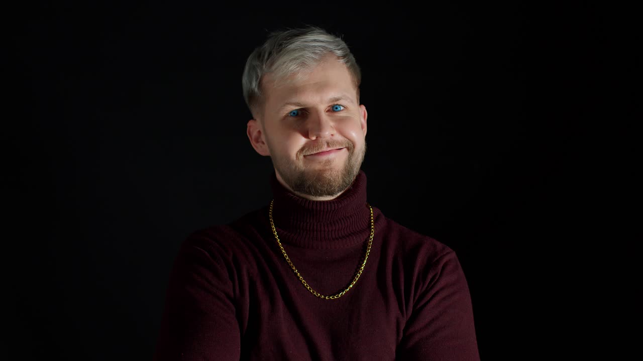 Smilende, glad ung mand i trendy, stilfuldt tøj med krydsede arme på sort baggrund.