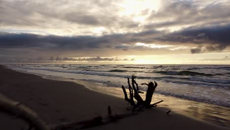 Beautiful-aerial-shot-flying-over-a-beach-at-sunset-on-the-Baltic-sea-coast,-high-contrast,-overcast-weather,-low-altitude-wide-angle-drone-shot-moving-forward-over-the-calm-waves