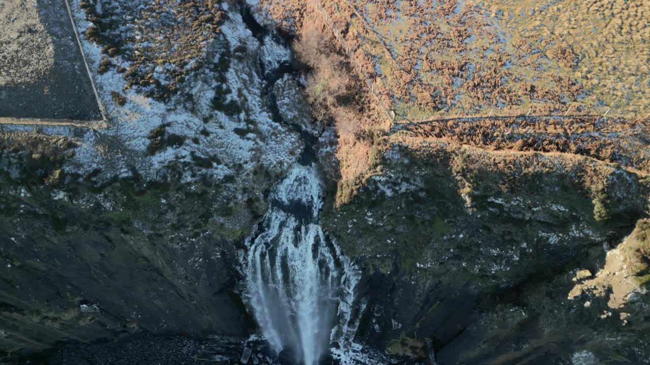 vuelo revelación de la cascada en cascada hacia abajo a la playa rocosa negra cubierta de helada, temprano en la mañana en invierno en la cascada de kilt rock, isla de skye, tierras altas occidentales, escocia, reino unido