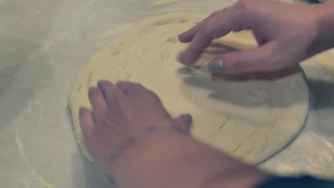 lady stretching and turning the pizza dough on the table with his bare hands