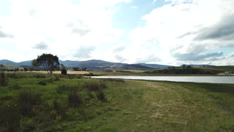 drone pan around native bushes to reveal water and country hillside and barn in tasmania, australia