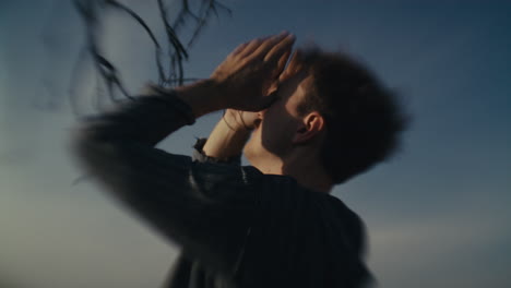 man with hands near face against blurry sky
