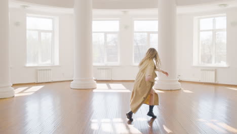 focused blonde woman in trench coat and boots training a contemporary dance in the middle of the studio 4